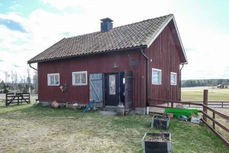 En röd träbyggnad med tegeltak används som gårdsbutik i ett öppet landskap under klarblå himmel.