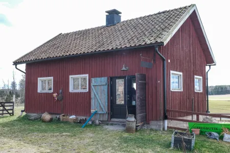 En traditionell röd gårdsbutik med tegeltak, öppen dörr och lantliga föremål utanför under tidig vår. (illustrationsbild)