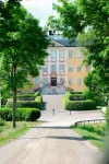 Eriksbergs slott syns rakt fram längs grusgången med gulvit fasad, dubbeltrappa och svensk flagga på taket.