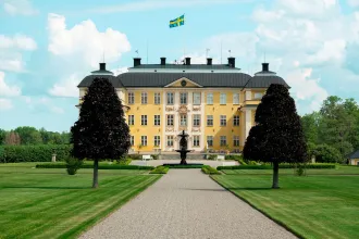 Eriksbergs slott längs grusgången med fontän och svensk flagga en sommardag.