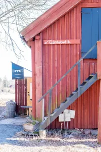 En röd träbyggnad med utvändig trätrappa och skyltar mot gårdsbutik under kal himmel. (illustrationsbild)