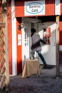 En person i grå kappa och mössa går in genom dörren till Barbros Café i en röd träbyggnad. (illustrationsbild)