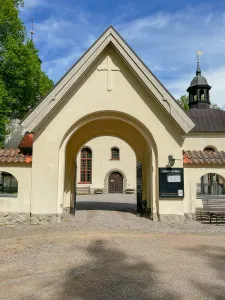 En putsad kyrkportal med kors ovanför valvet öppnar mot Julita kyrkas dörr och fönster en solig dag. (illustrationsbild)