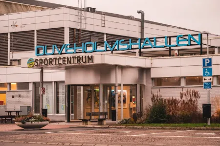 Entrén till Duveholmshallen och Sportcentrum syns från gatan med parkering i förgrunden.