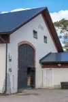 En vit ekonomibyggnad med röd träpanel och årtalet 2010 på gaveln ovanför en stor svart välvd port.