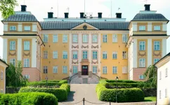 Hela huvudfasaden på Eriksbergs slott med flyglar, klippta häckar och grusgång under klar sommarhimmel.