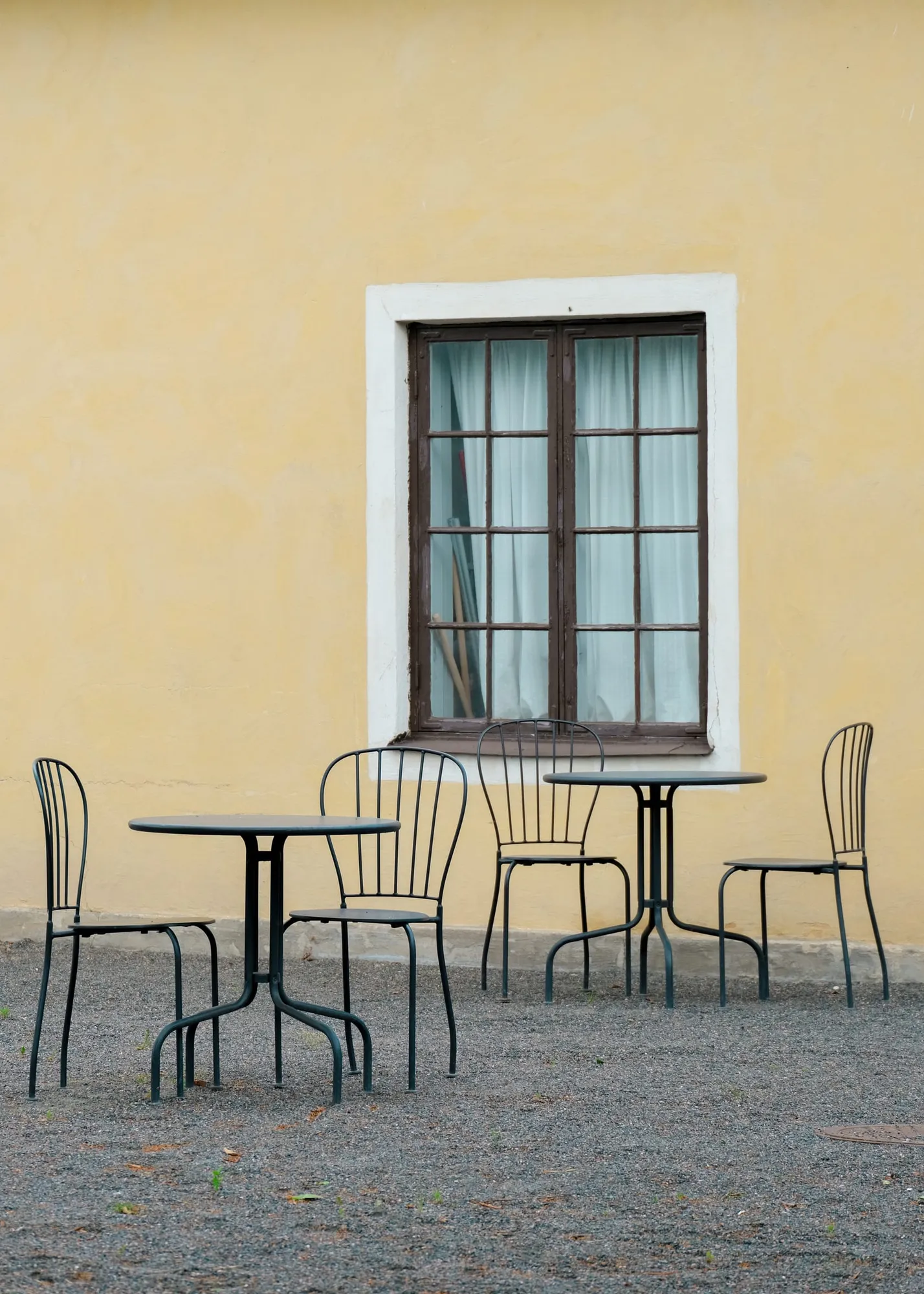Schwarze Caféstühle und runde Tische auf Kies vor einer gelben Wand in Eriksberg.